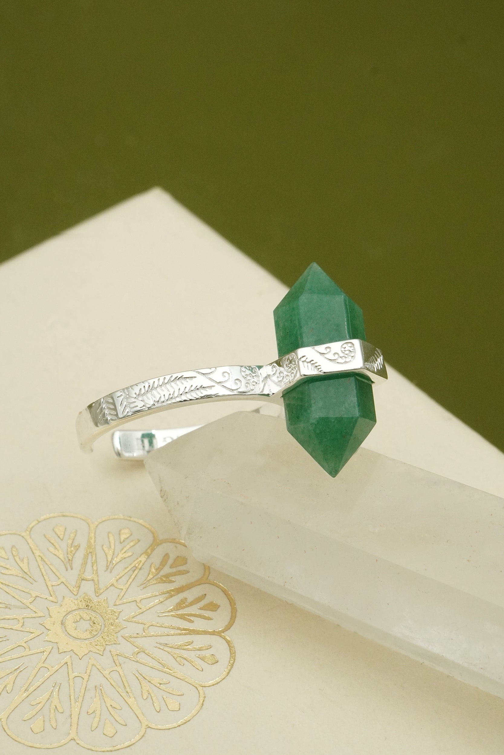 Silver ring with a green crystal on a beige surface with a green background