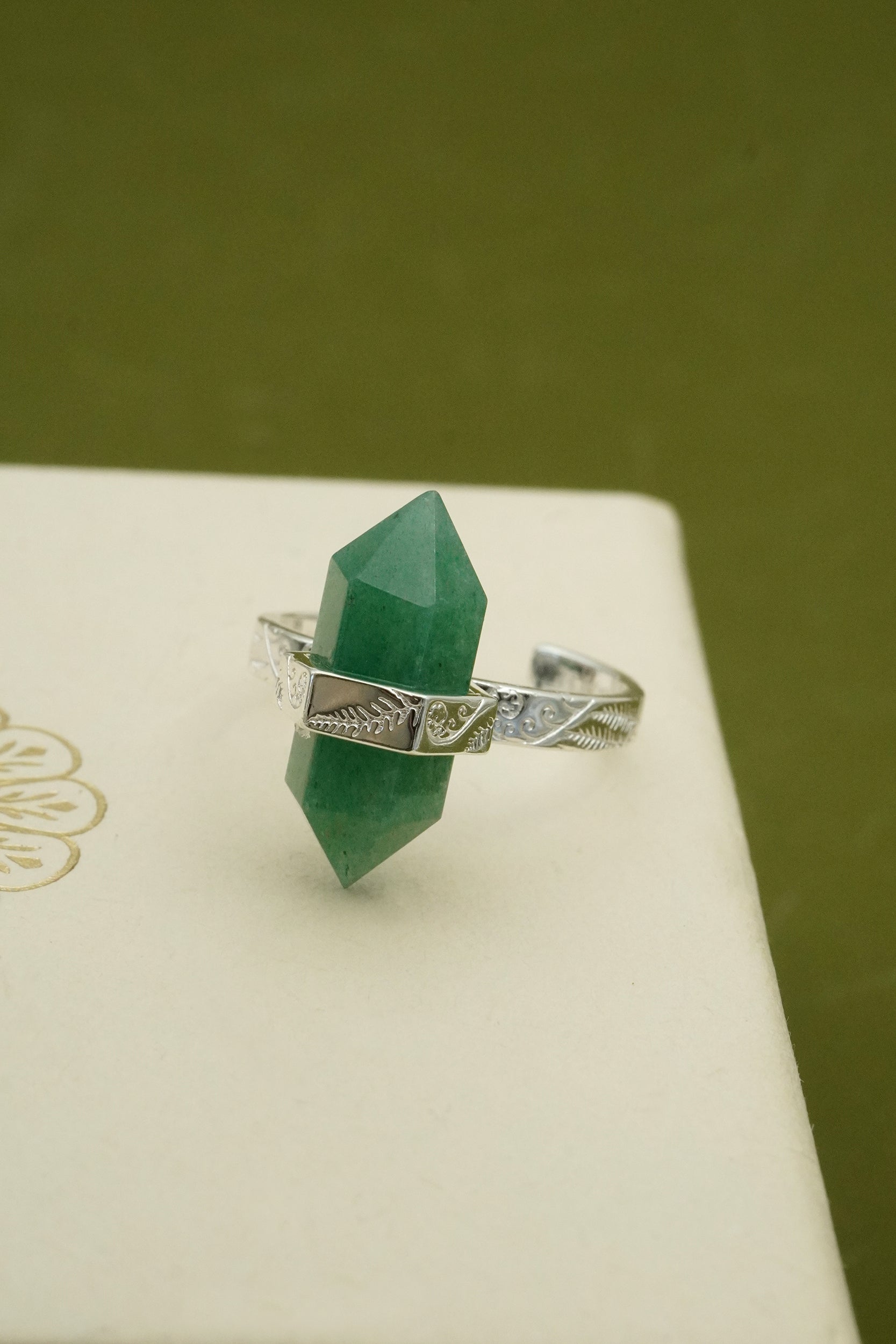 Silver ring with a green crystal on a white surface with a green background