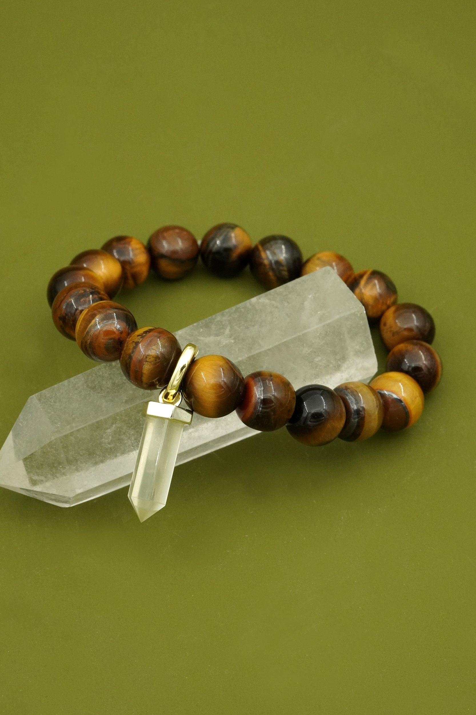 Bracelet with tigers eye crystal beads and a gold citrine charm on a green background