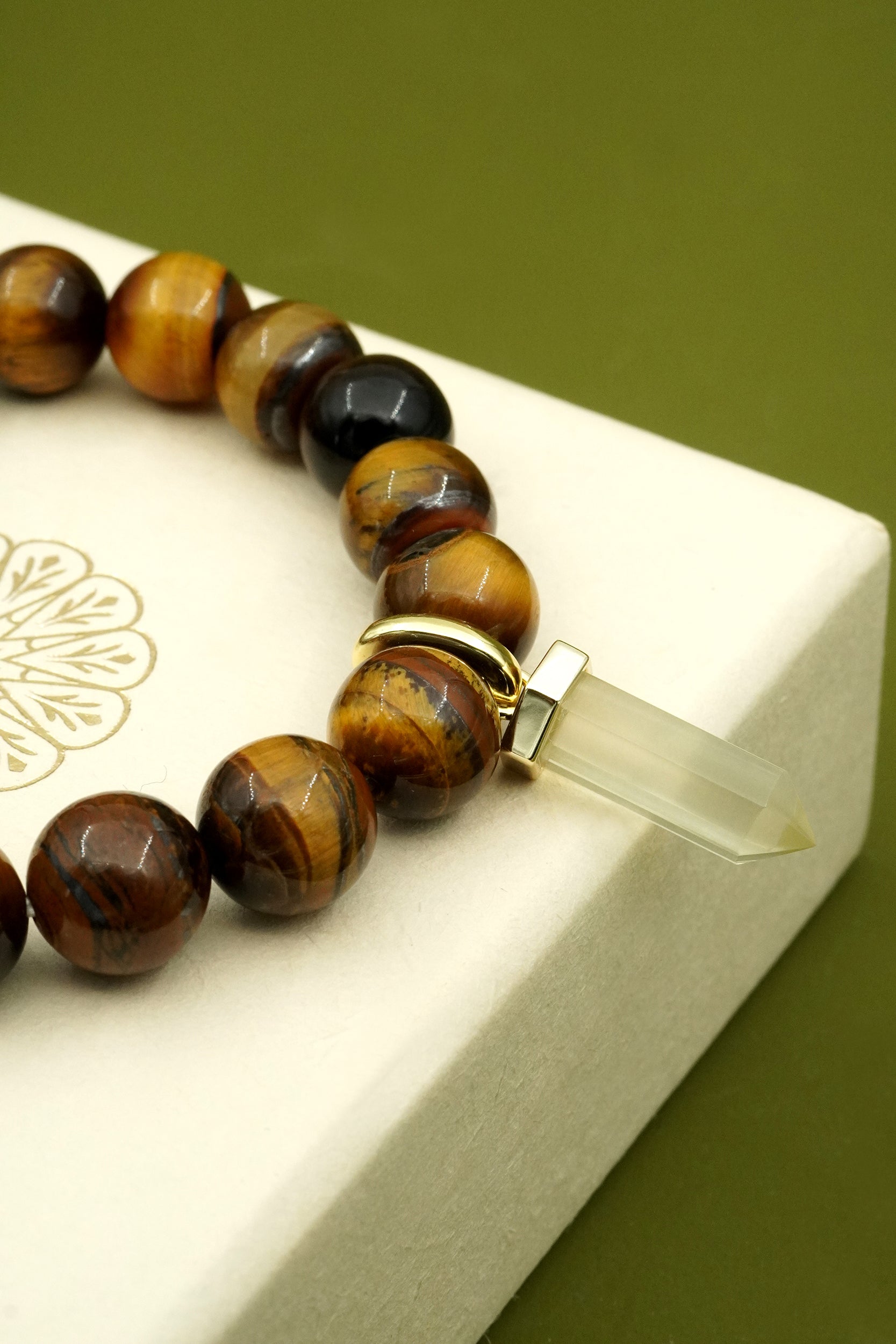Tiger's Eye crystal beaded bracelet with a citrine crystal charm on a white box with gold design