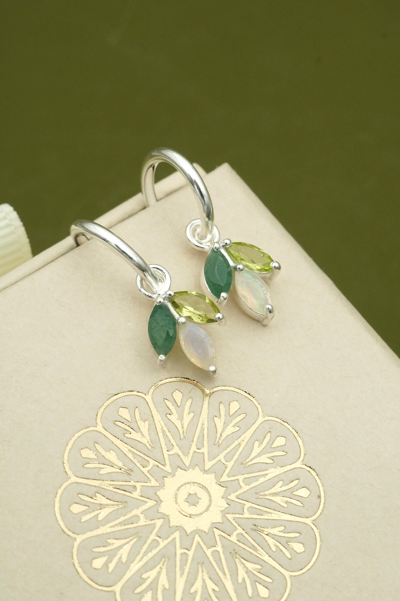 Silver earrings with green and opal gemstones on a decorative box with a floral design.