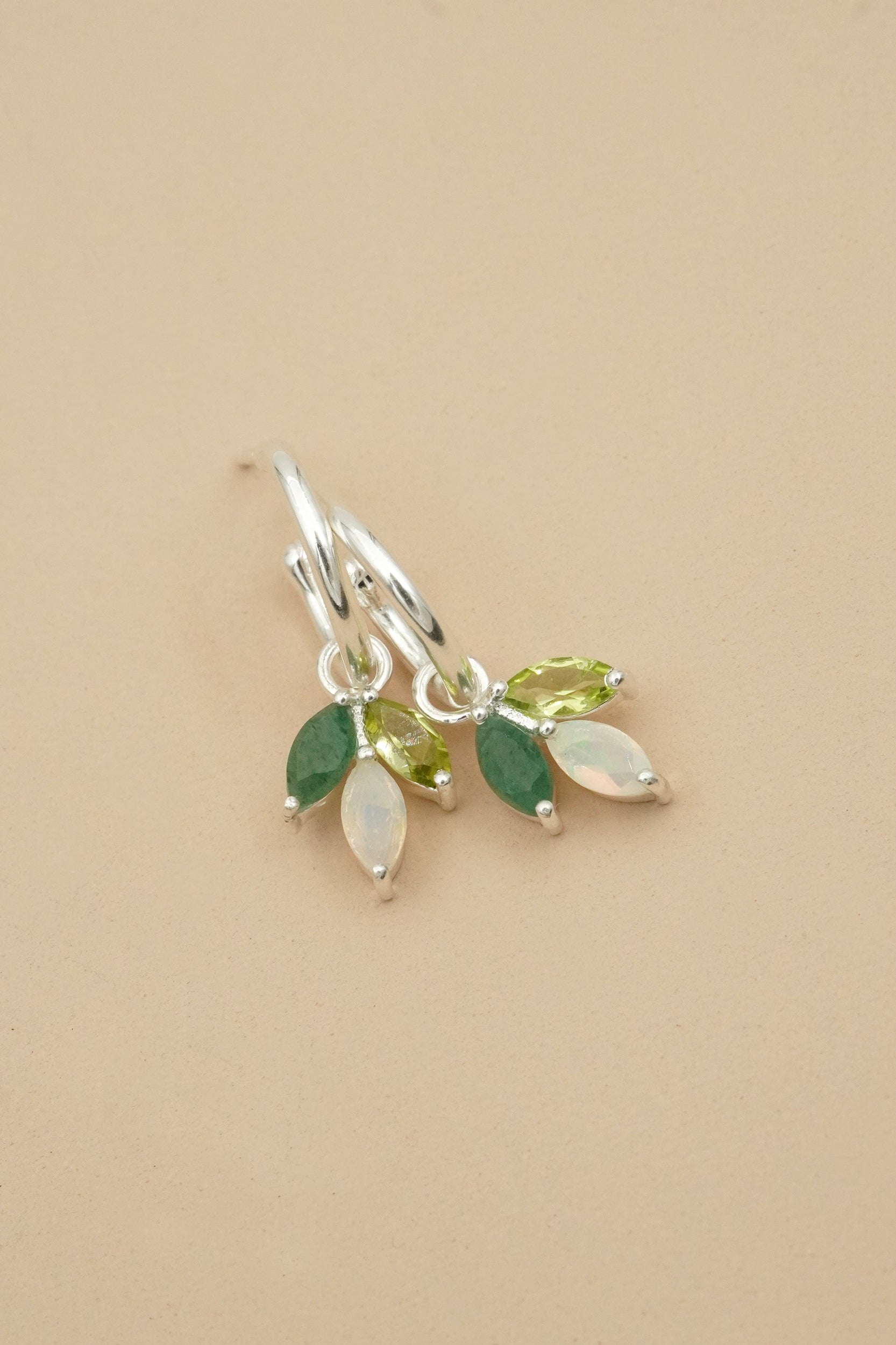 Silver earrings with green and opal leaf-shaped stones on a beige background