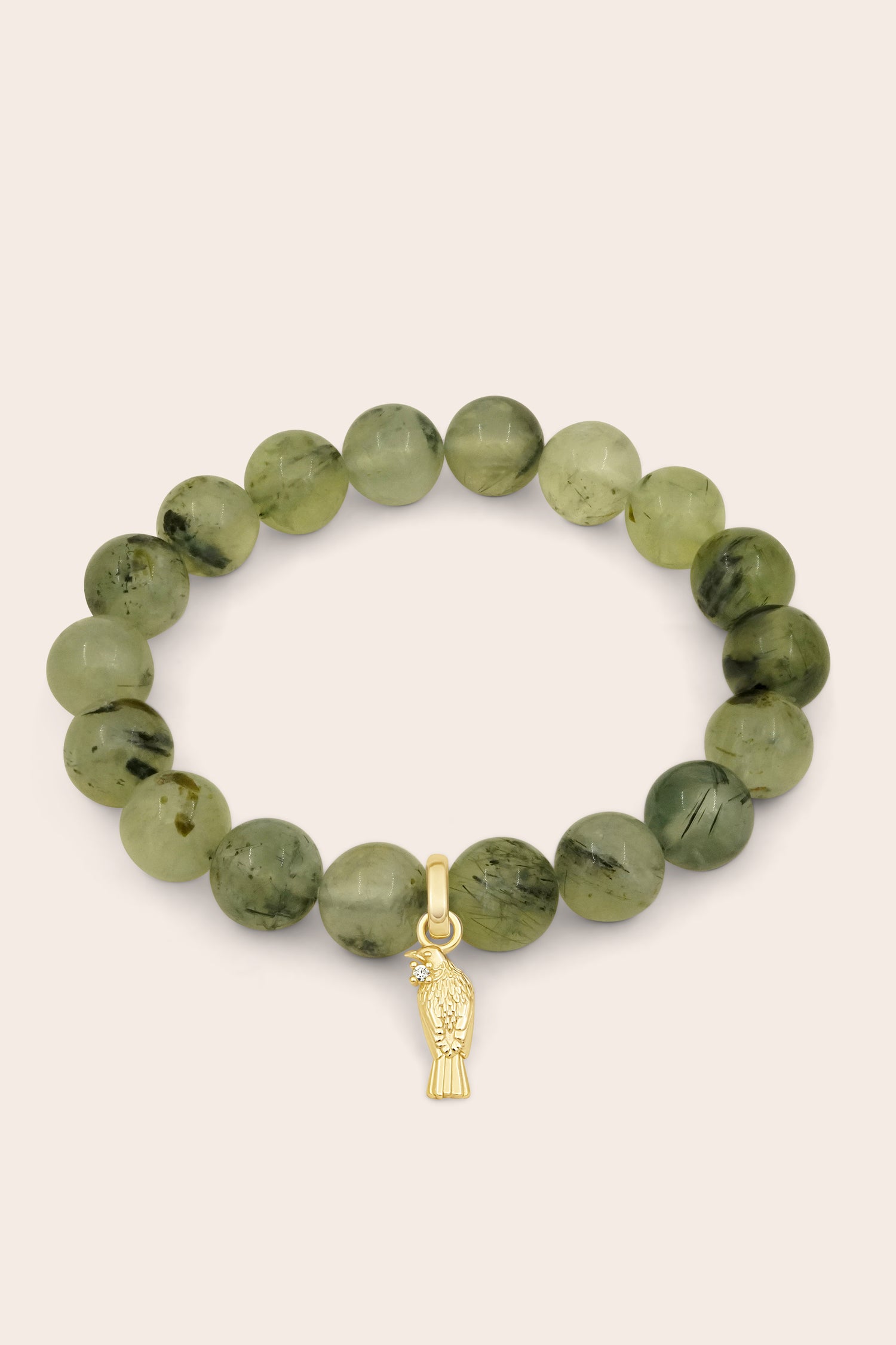 Green beaded gemstone bracelet with a gold Tui charm on a beige background