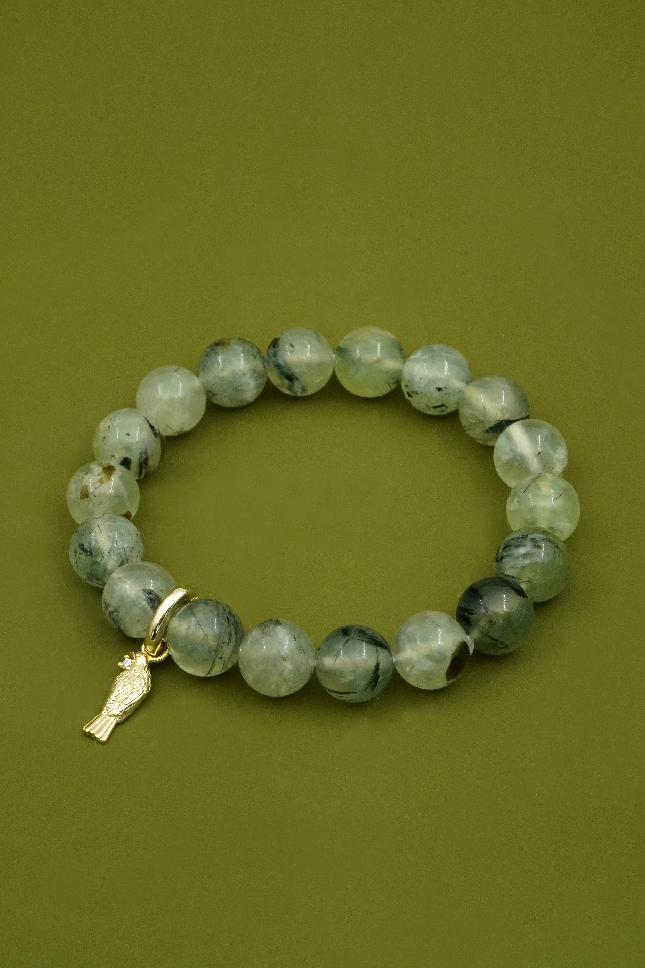 Green beaded gemstone bracelet with a gold NZ Tui bird charm on a green background