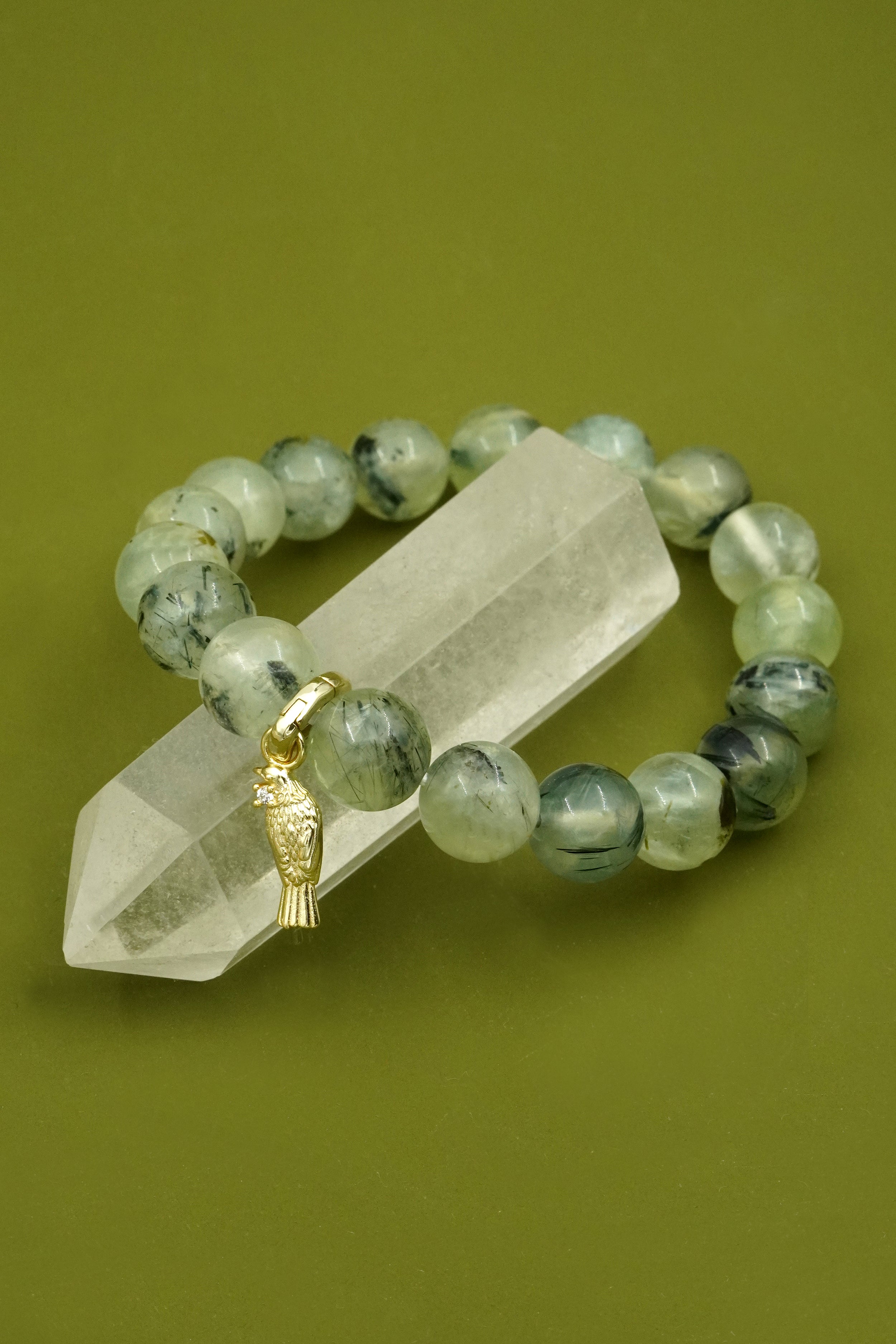 Green beaded bracelet with a gold native NZ Tui bird charm on a clear crystal on a green background