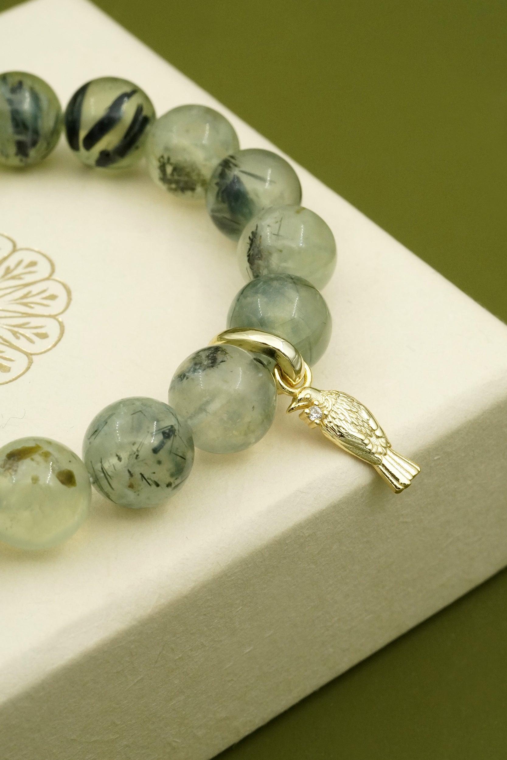 Green beaded bracelet with a gold Tui charm on a white jewellery box