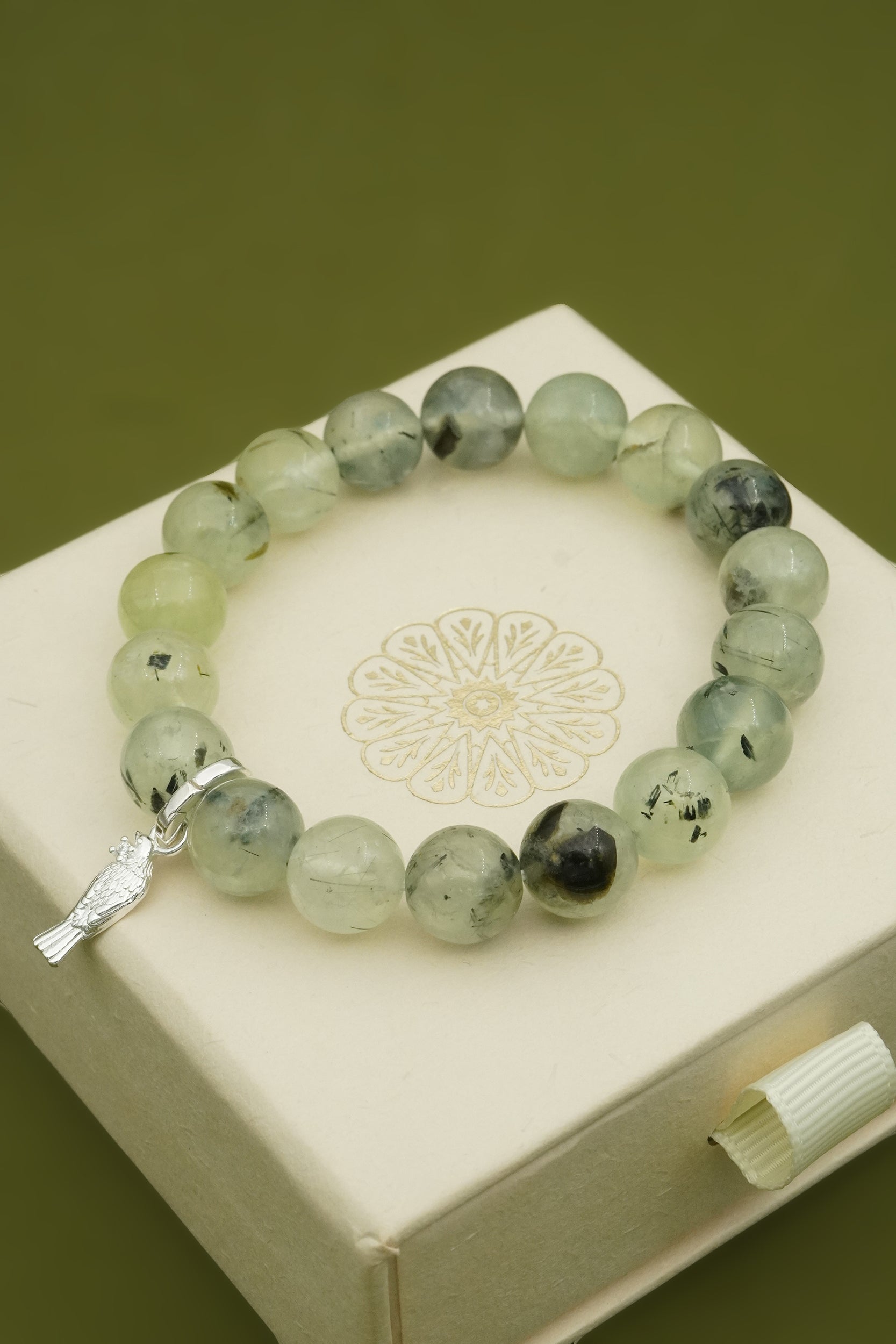 Green beaded bracelet with a silver native NZ Tui bird charm on a white box with a floral design.