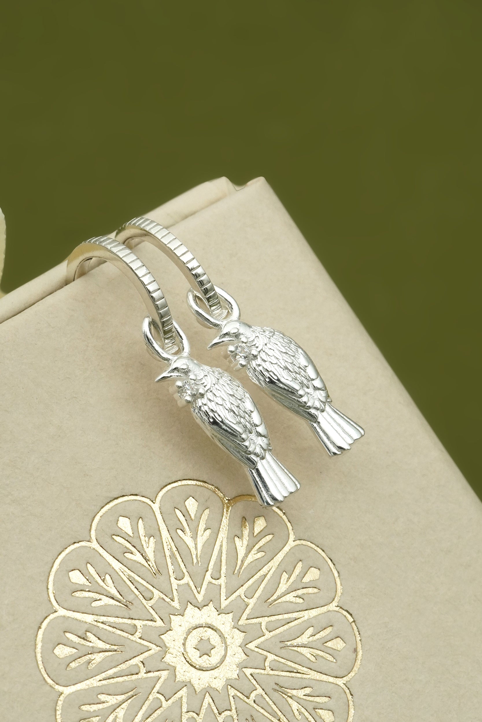 Silver tui NZ bird-shaped earrings on a beige card with floral design