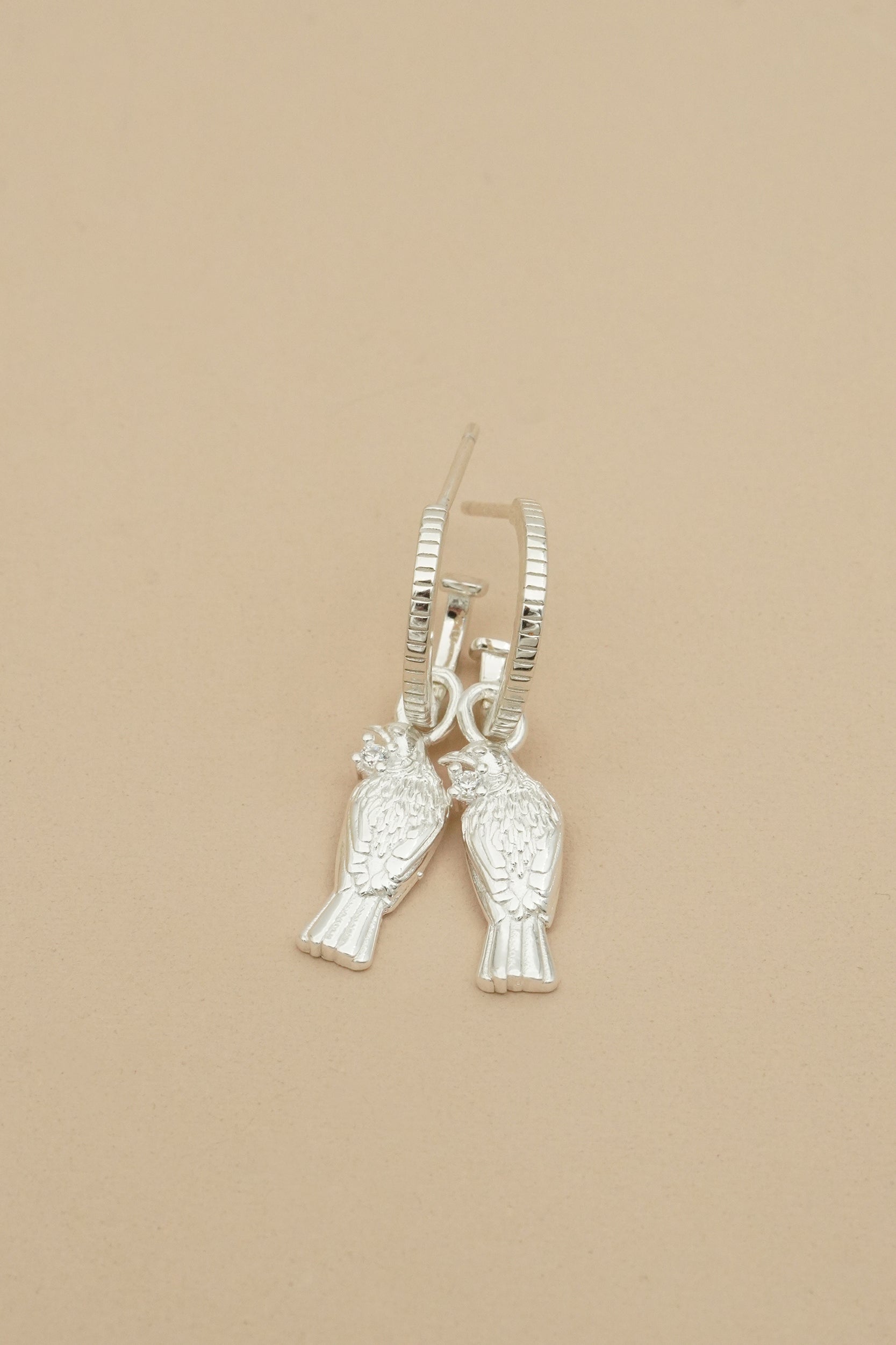 Silver Tui bird-shaped hoop earrings on a beige background