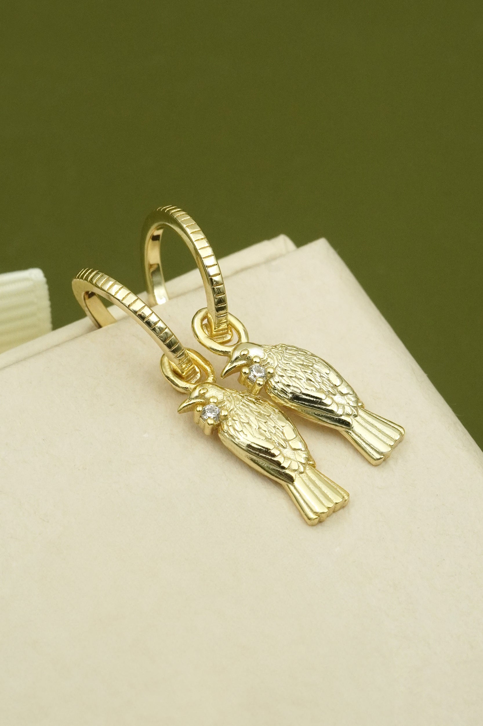 Gold tui bird-shaped earring on a beige stand with a green background