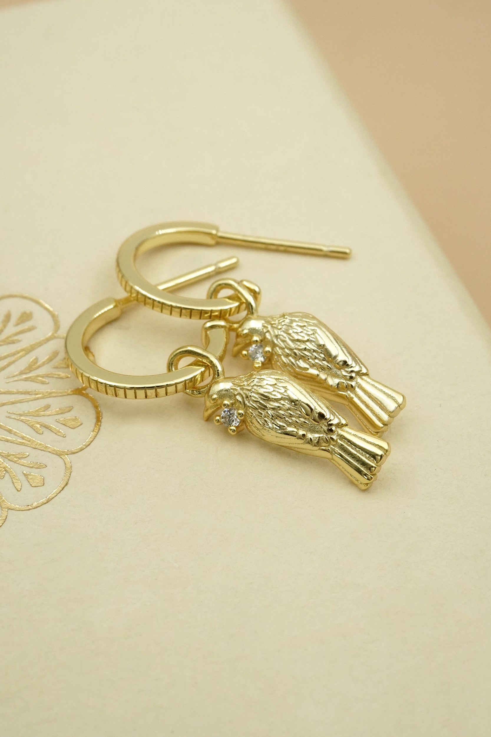 Gold Tui native NZ bird earrings on a beige background