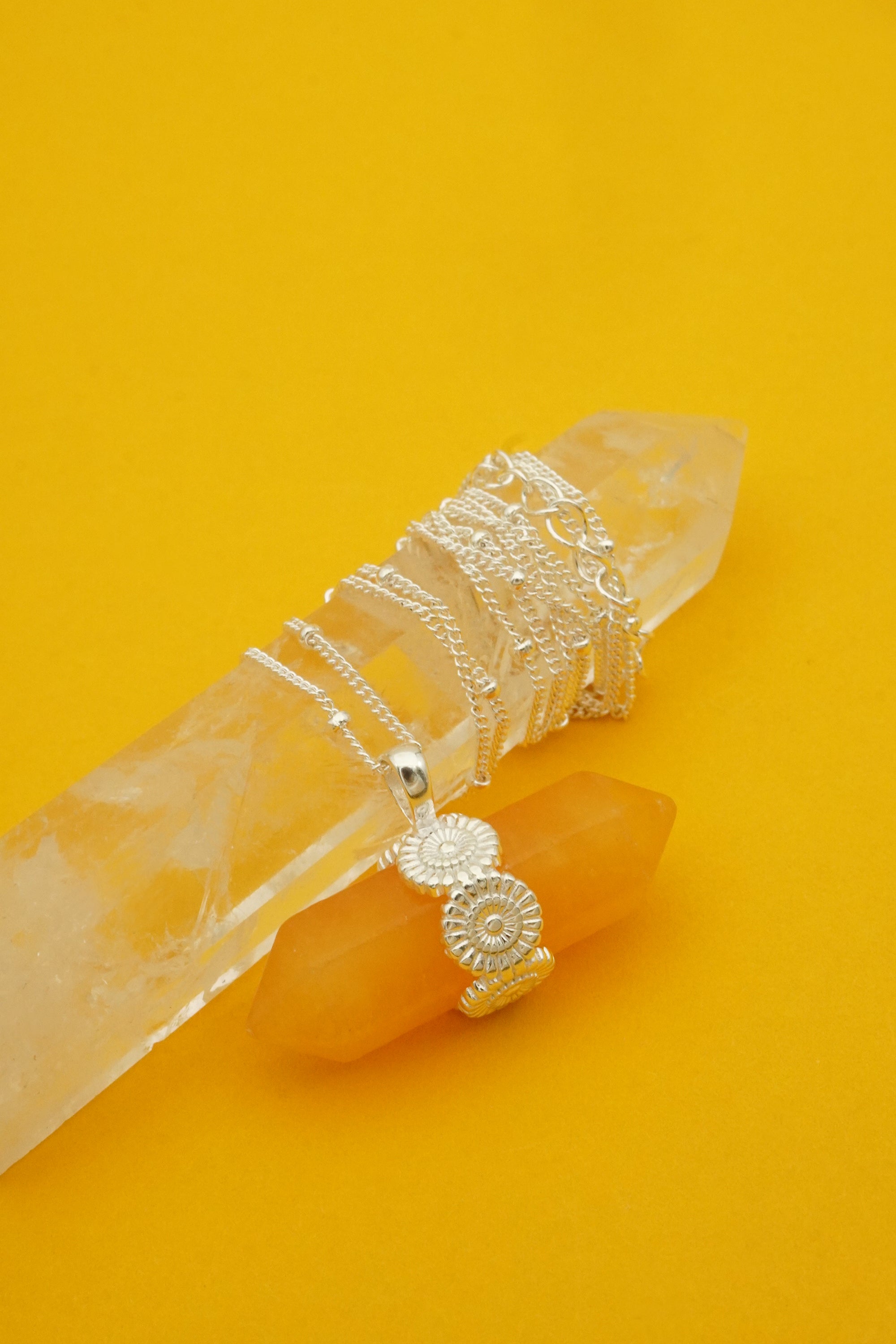 Silver jewellery set including rings and a necklace on a clear crystal with a yellow background
