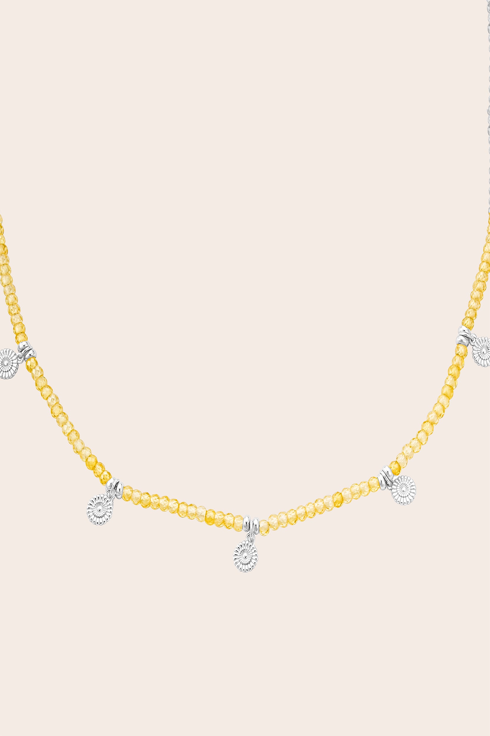 Yellow beaded necklace with silver flower pendants on a beige background