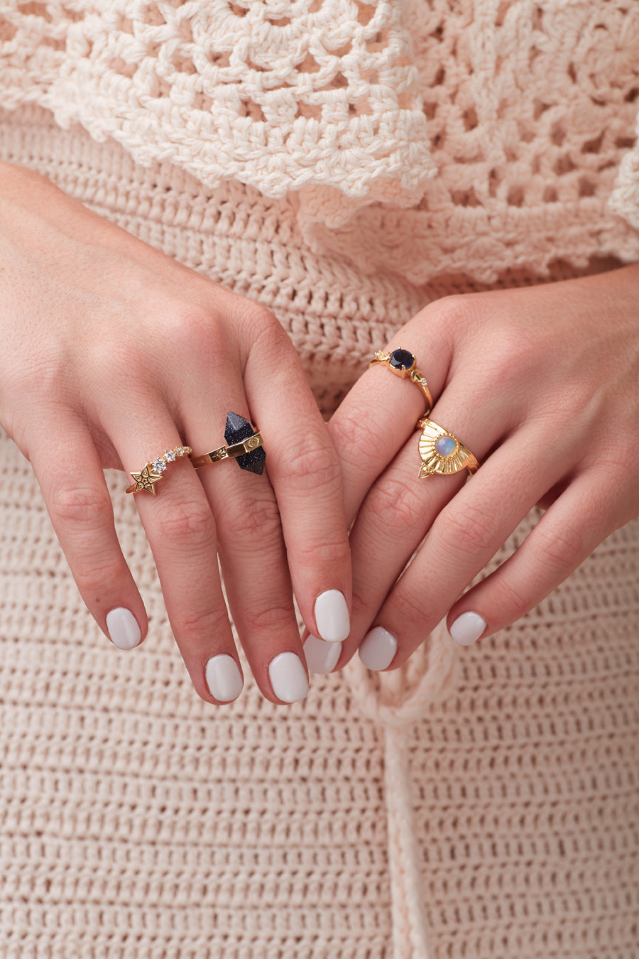 Opal ring and other gemstone rings being worn on hands over cream crochet dress